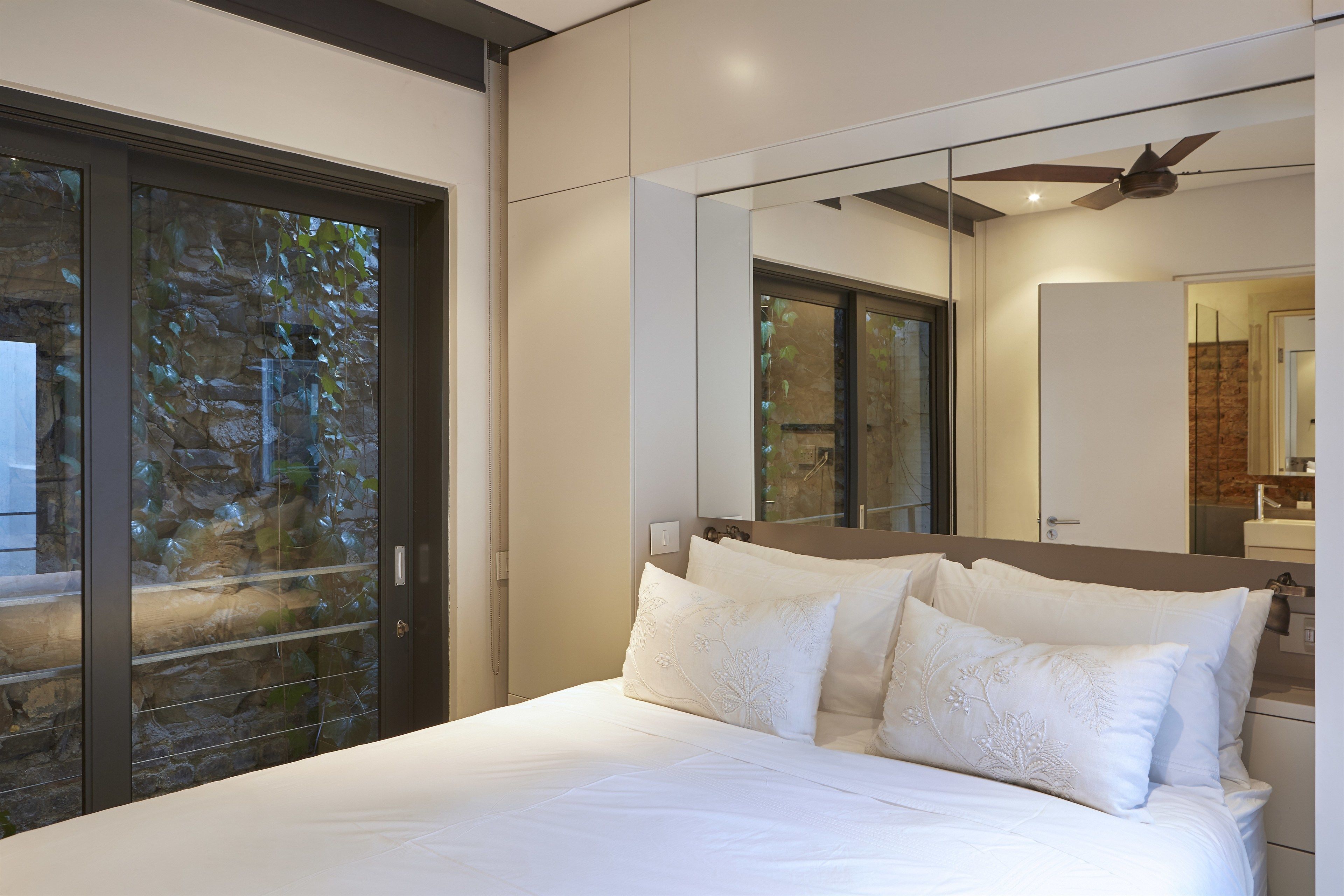 Una camera da letto moderna con un letto grande, una ventola a soffitto e una porta in vetro che dà su un muro in pietra.