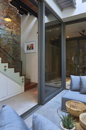 A modern interior with a staircase, a glass door leading to a balcony, and a seating area with cushions and a wooden table.