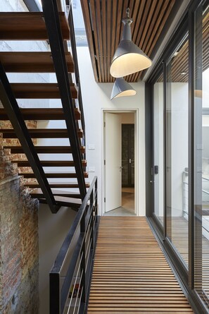 A modern interior with a wooden staircase, a glass door leading to a balcony, and a pendant light.