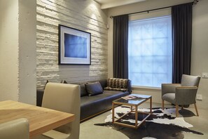 A modern living room with a sofa, a coffee table, and a chair. There is a window with curtains, a framed picture on the wall, and a cowhide rug.