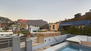 Ein Poolbereich auf dem Dach mit Blick auf einen Berg, einer Holzterrasse und einem blauen Gebäude.
