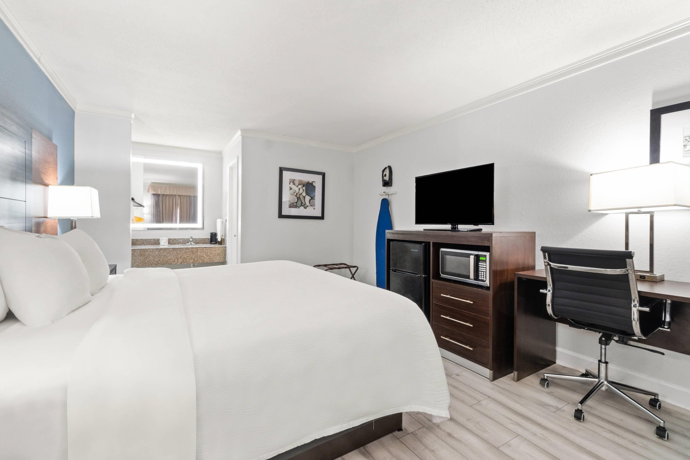 Een hotelkamer met een groot bed, een bureau met een computer, een televisie en een magnetron.