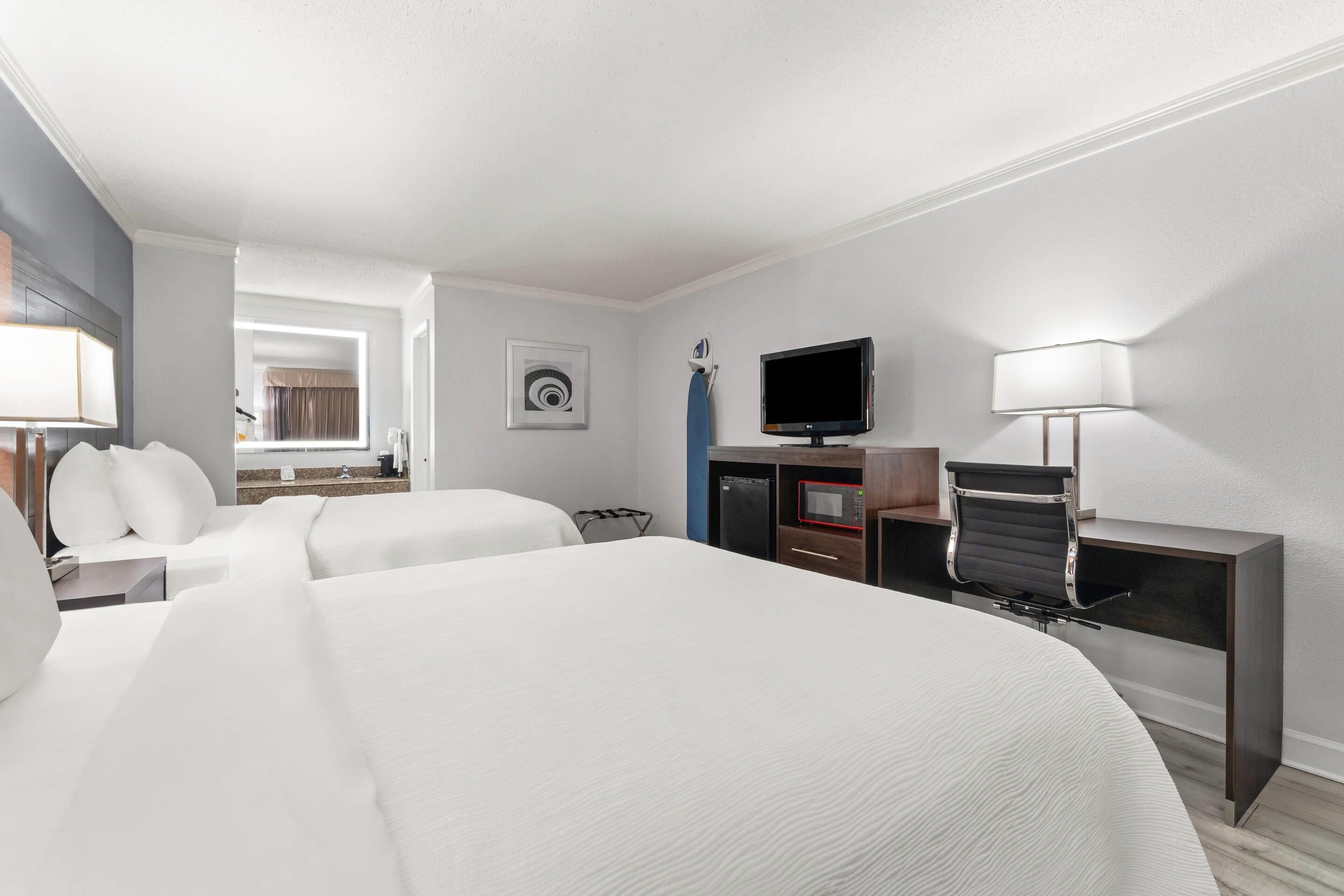 Habitación de hotel con dos camas, un escritorio con silla, una televisión y una lámpara.