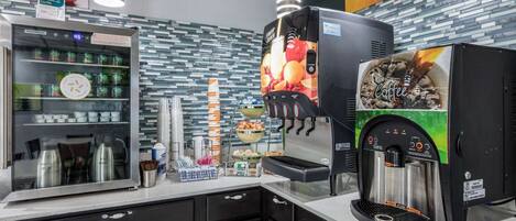 Una estación de café con una máquina de café, un dispensador de bebidas y un refrigerador con vasos y un reloj.