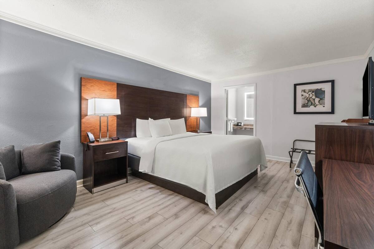 Ein Hotelzimmer mit Bett, Nachttischen, einem Sessel, Schreibtisch, Lampe, Spiegel und Fernseher.