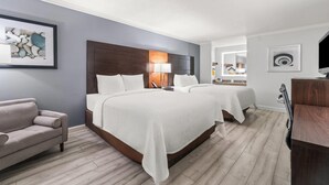 Une chambre d’hôtel avec deux lits, un canapé, un bureau et des œuvres d’art accrochées aux murs.