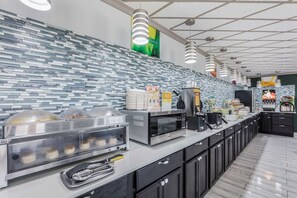 A modern kitchen with a tiled backsplash, stainless steel appliances, and a long counter with various food items and utensils.