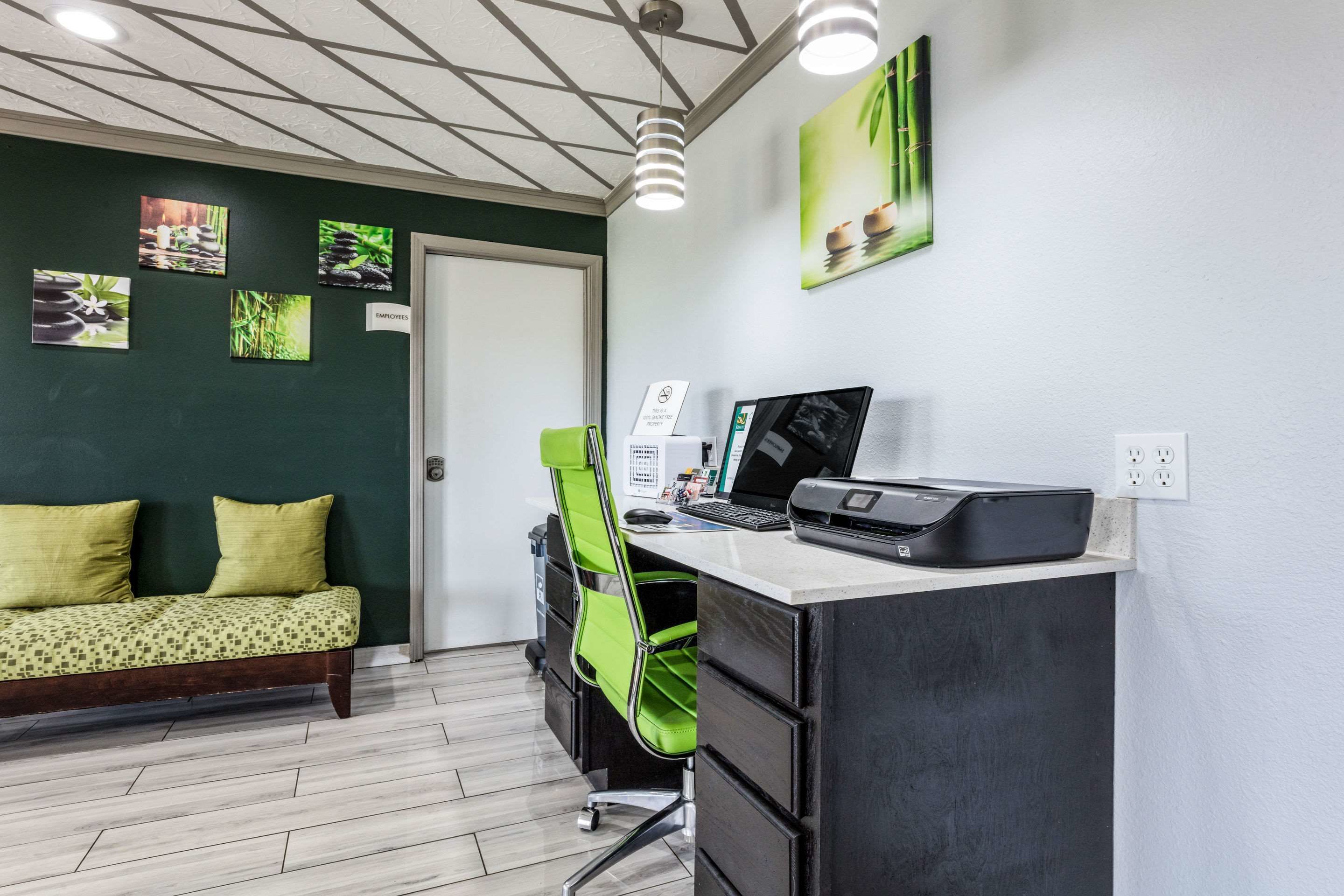 Una habitación con escritorio, una silla verde, un sofá con cojines y decoración en la pared.
