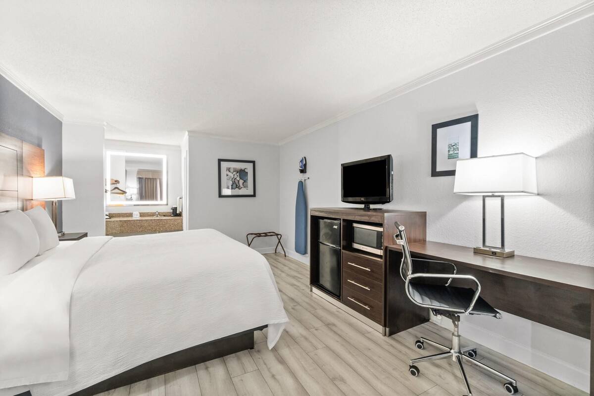 Ein Hotelzimmer mit einem großen Bett, einem Schreibtisch mit Stuhl, einem Fernseher und einem durchgegangenes Badezimmer.