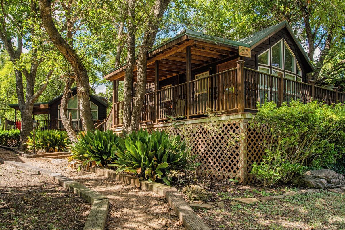 A cabin with a wooden deck, surrounded by trees and plants.