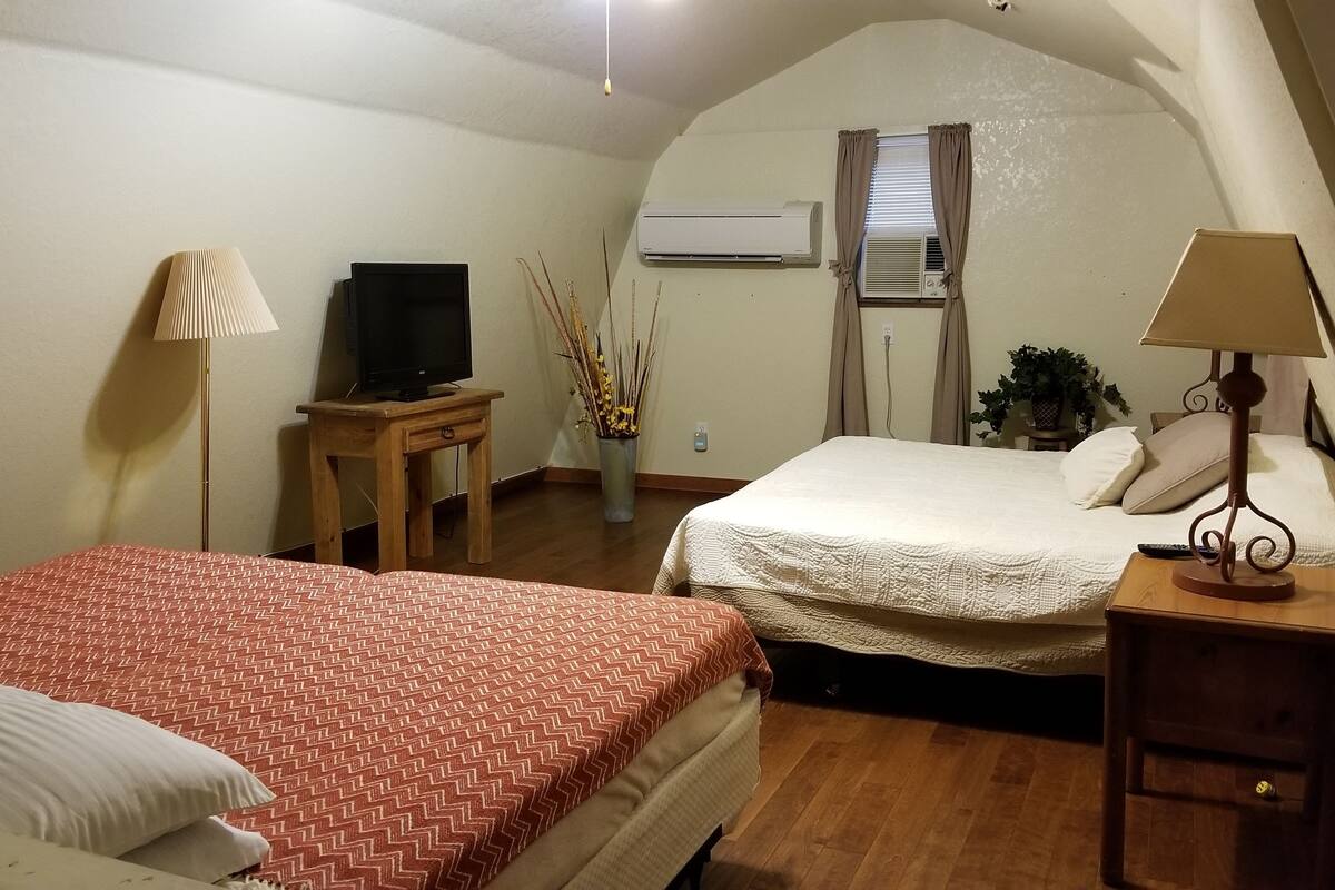 A hotel room with two beds, a television, an air conditioning unit, and a lamp.
