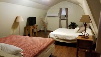 A hotel room with two beds, a television, an air conditioning unit, and a lamp.