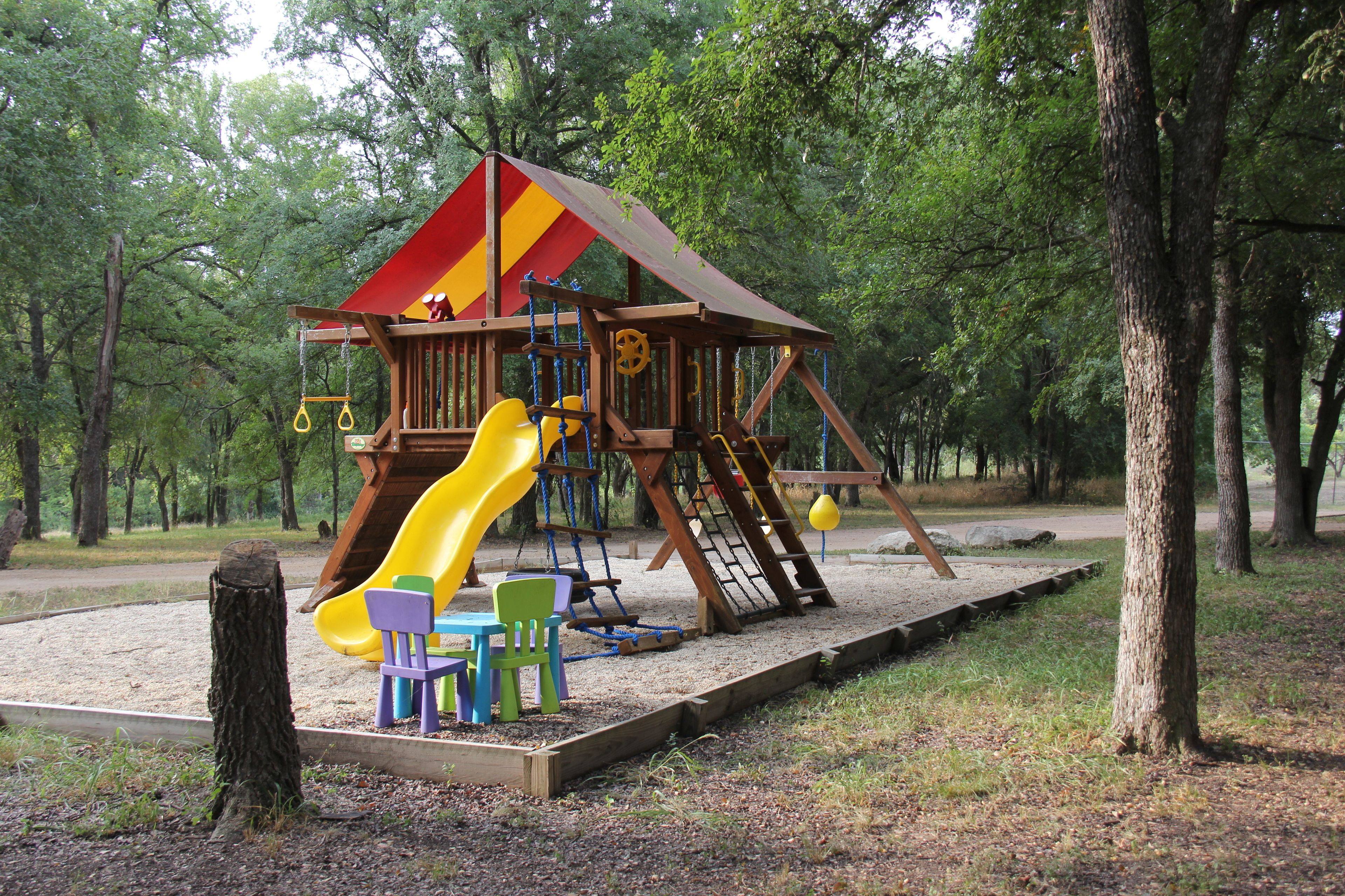 Una estructura de madera para juegos con un tobogán y elementos de escalada, rodeada de árboles.