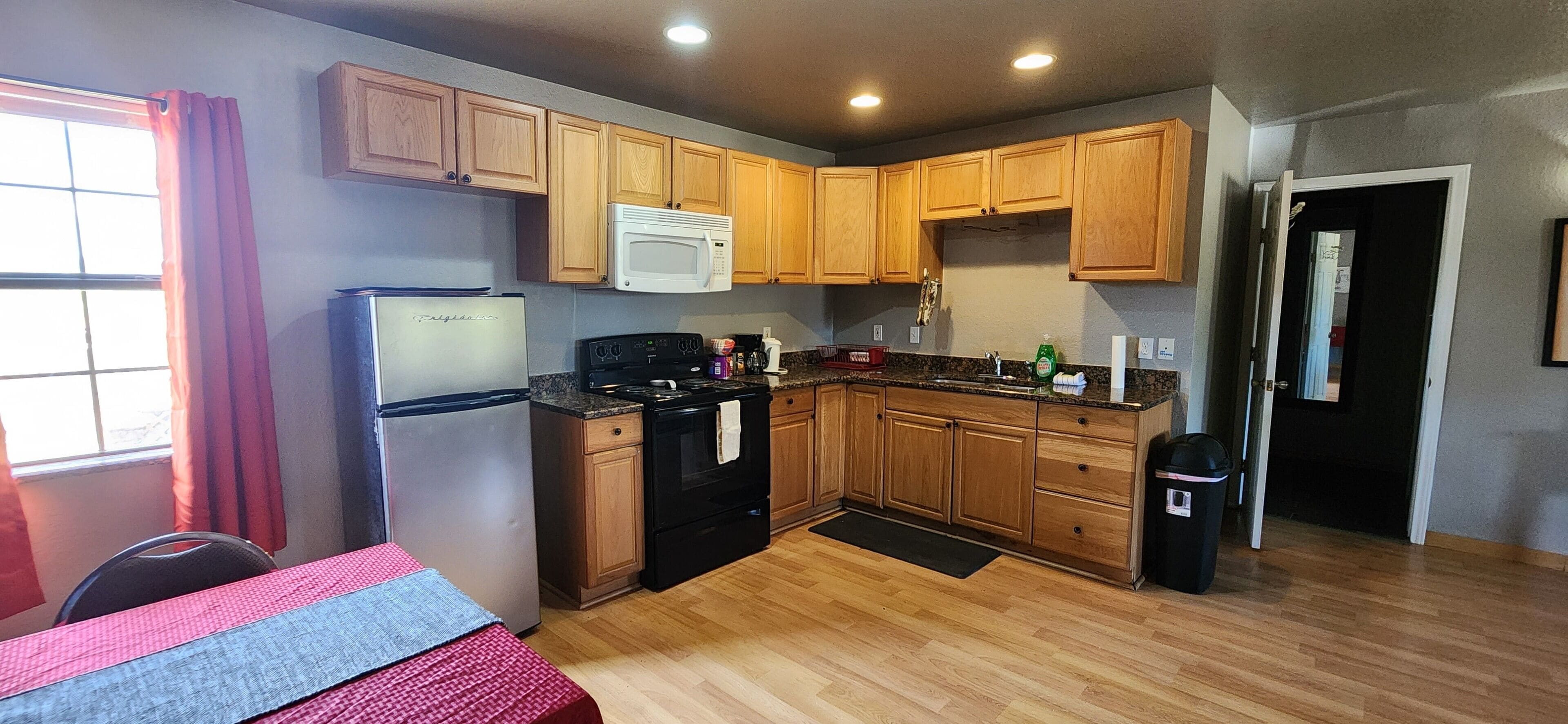 A compact kitchen with wooden cabinets, a refrigerator, a microwave, and a stove.