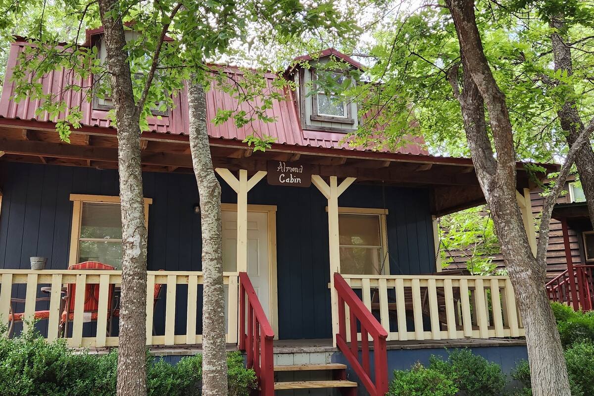 A cabin with a porch, a red staircase, and a window with a view of the surrounding trees.