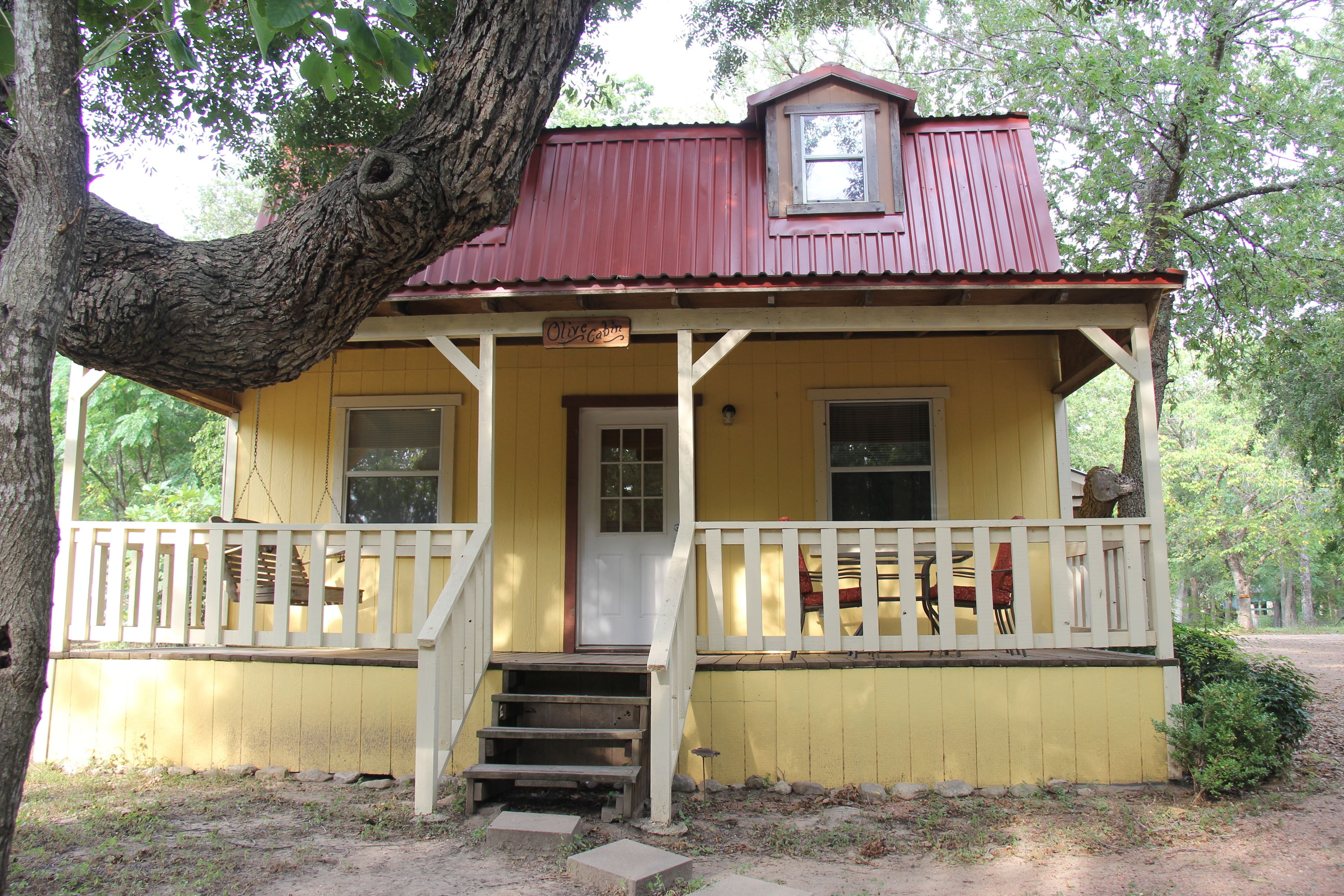 A yellow building with a red roof, a porch with white railings, and a small window above the door.