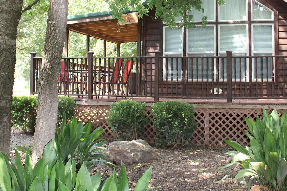 A wooden cabin with a porch, surrounded by trees and plants.