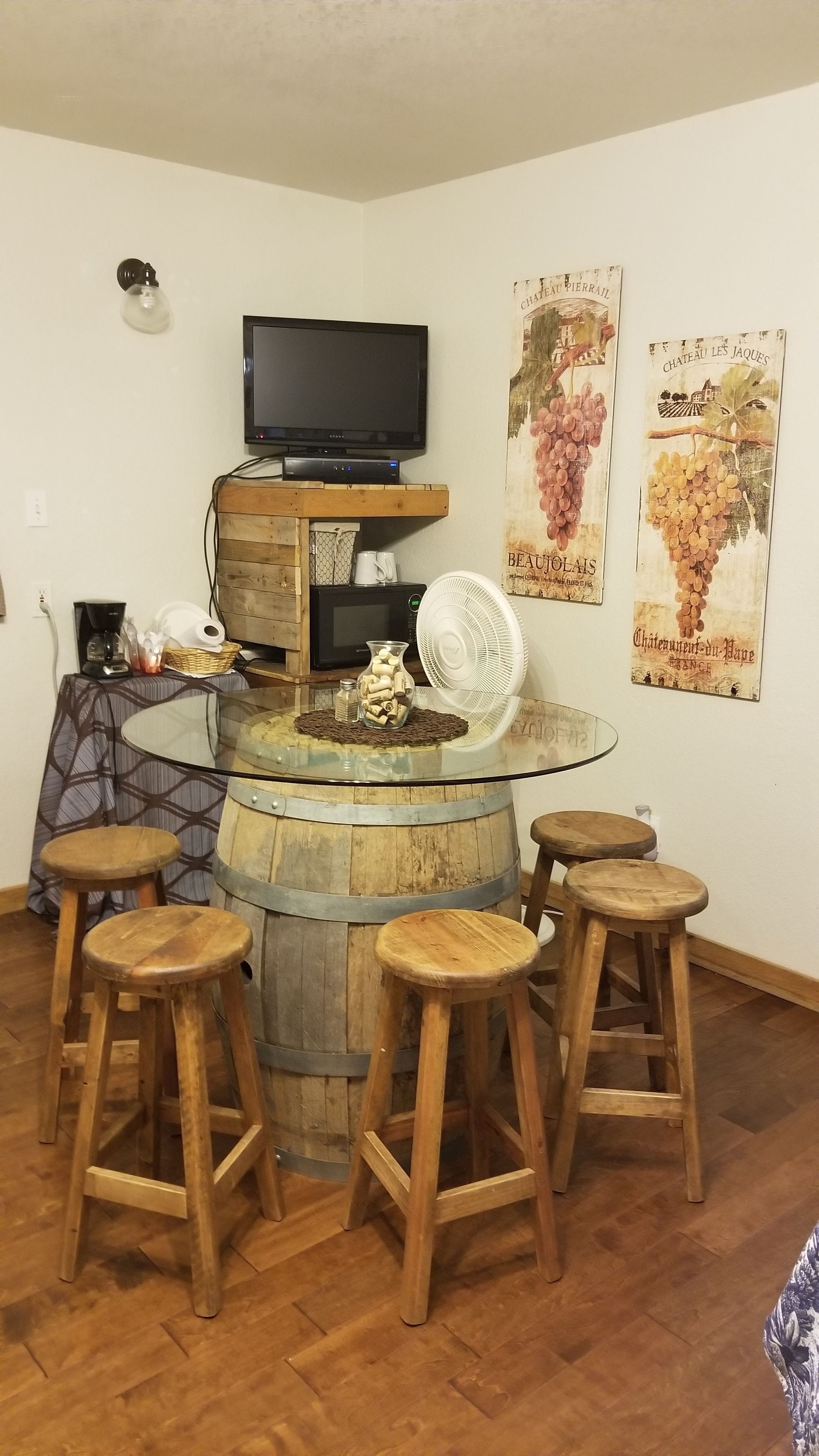 A bar area with a wooden barrel table, four wooden stools, a television, and vintage posters on the wall.