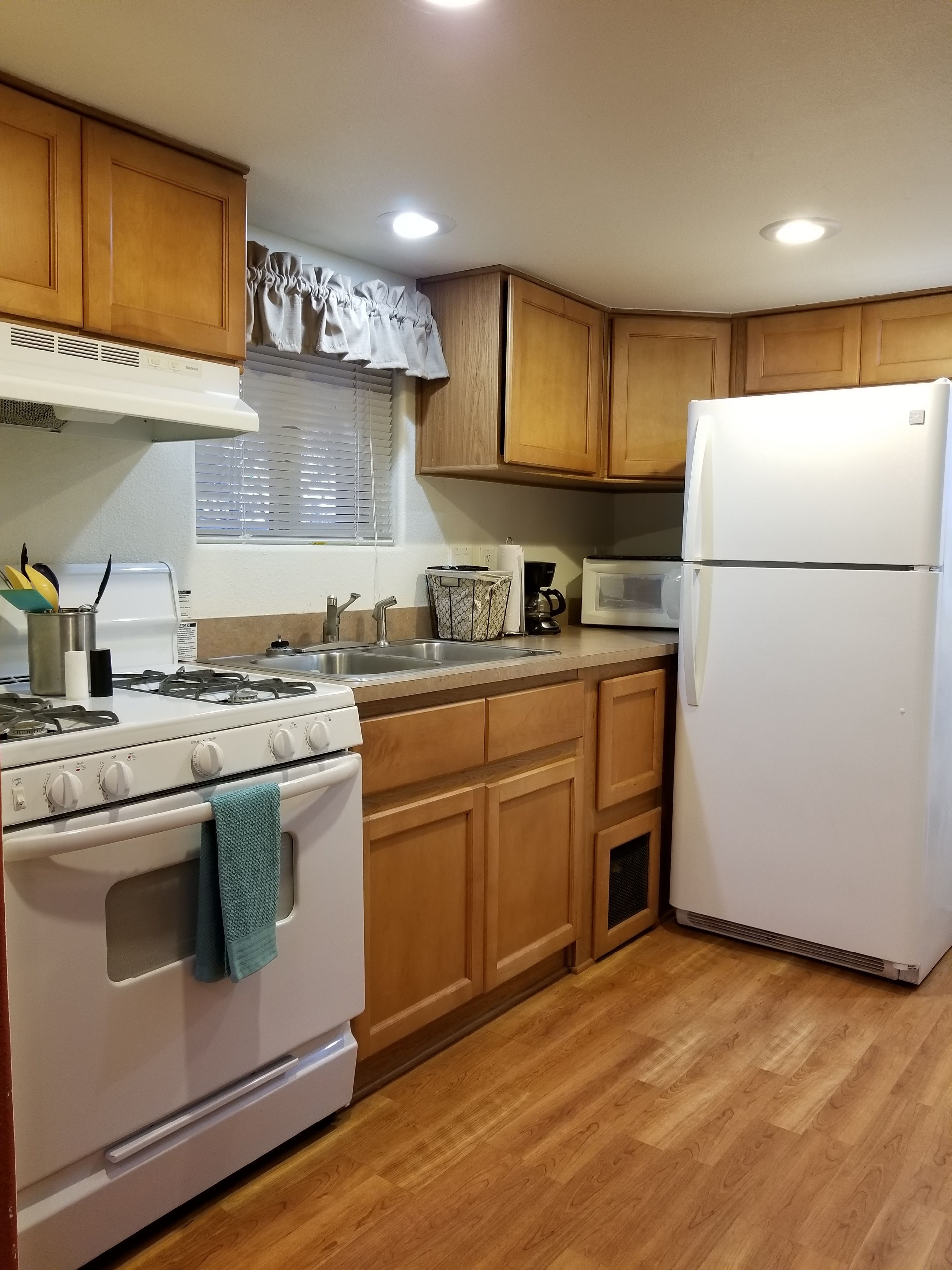 A kitchen with wooden cabinets, a white stove, a white refrigerator, and a window with blinds.