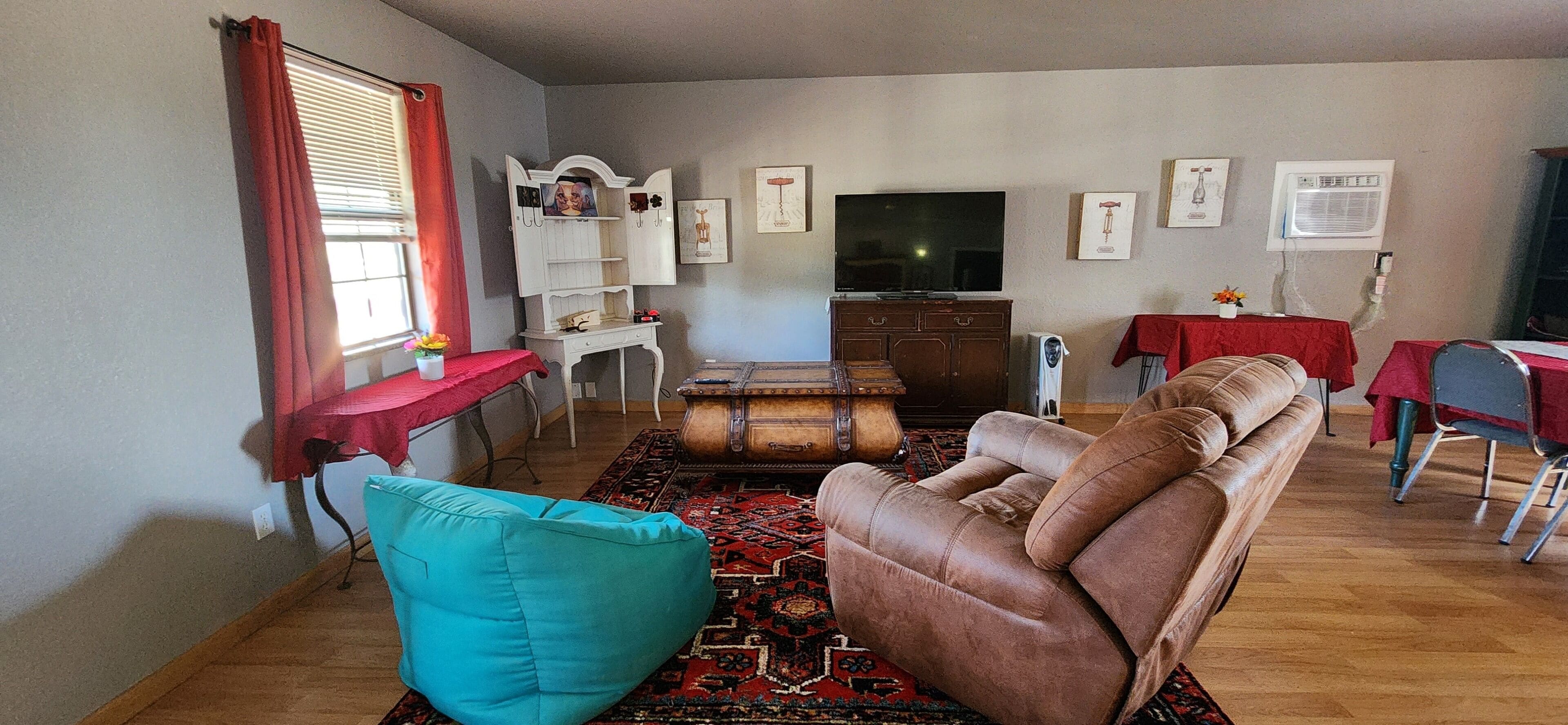 Un salon avec un canapé en cuir marron, un fauteuil turquoise, une table basse en bois et un téléviseur posé sur un meuble.