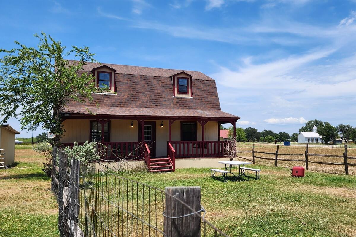 A two-story house with a porch, a fenced yard, and a picnic table.