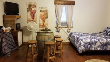 Une petite pièce agréable et chaleureuse, avec un lit, une table en bois et des tabourets, un téléviseur et des œuvres d’art accrochées au mur.