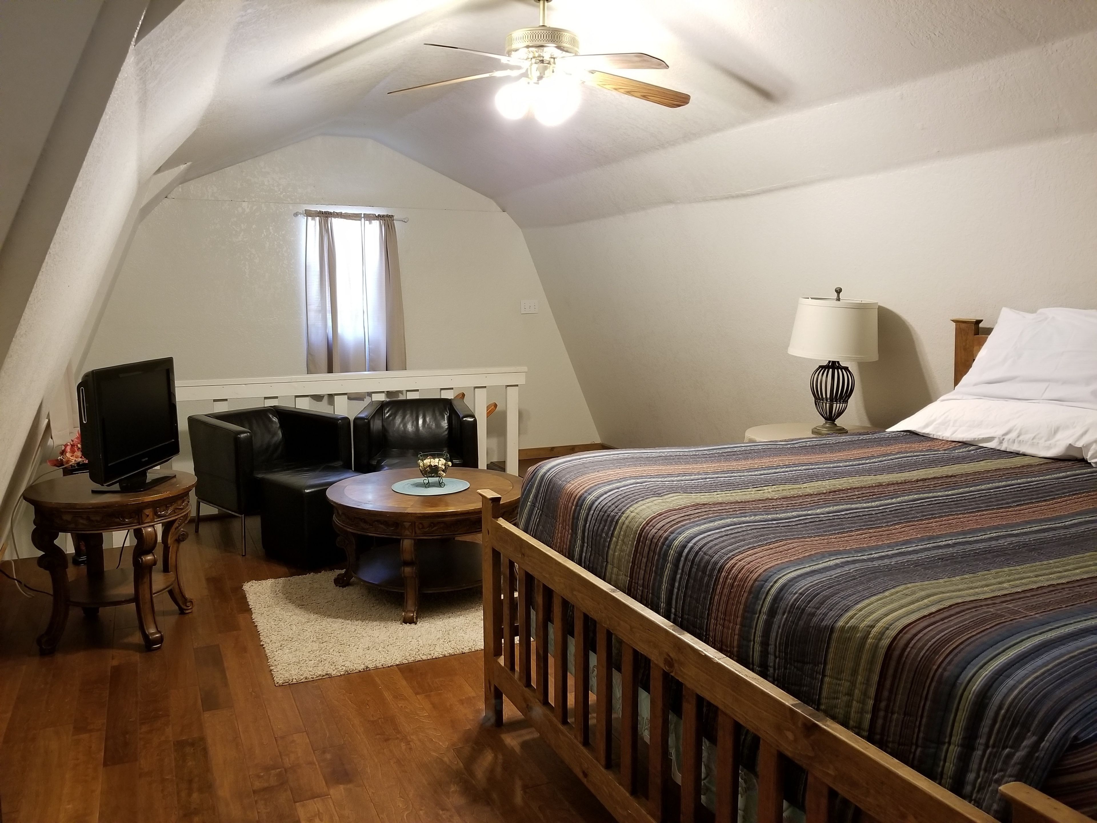 A cozy attic bedroom with a bed, a desk with a computer, a chair, and a ceiling fan.