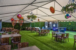 A tented outdoor dining area with tables and chairs, hanging decorations, and a green wall with sunflowers. - The Newmachar Hotel (Aberdeen)