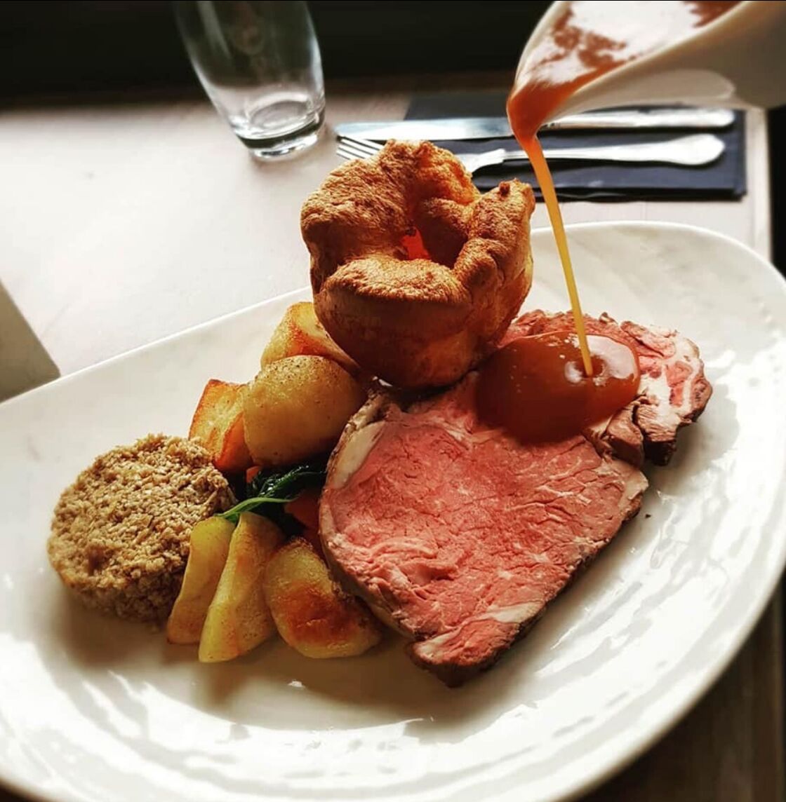 A plate of food including roast beef, Yorkshire pudding, and roasted potatoes.