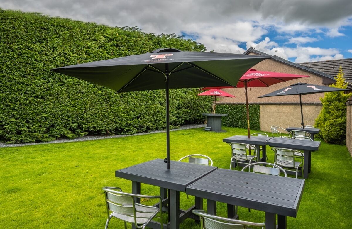 An outdoor patio area with tables and chairs, surrounded by a well-maintained lawn and a hedge.