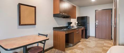 A compact kitchen with a dining table and chairs, a refrigerator, and wooden cabinets.