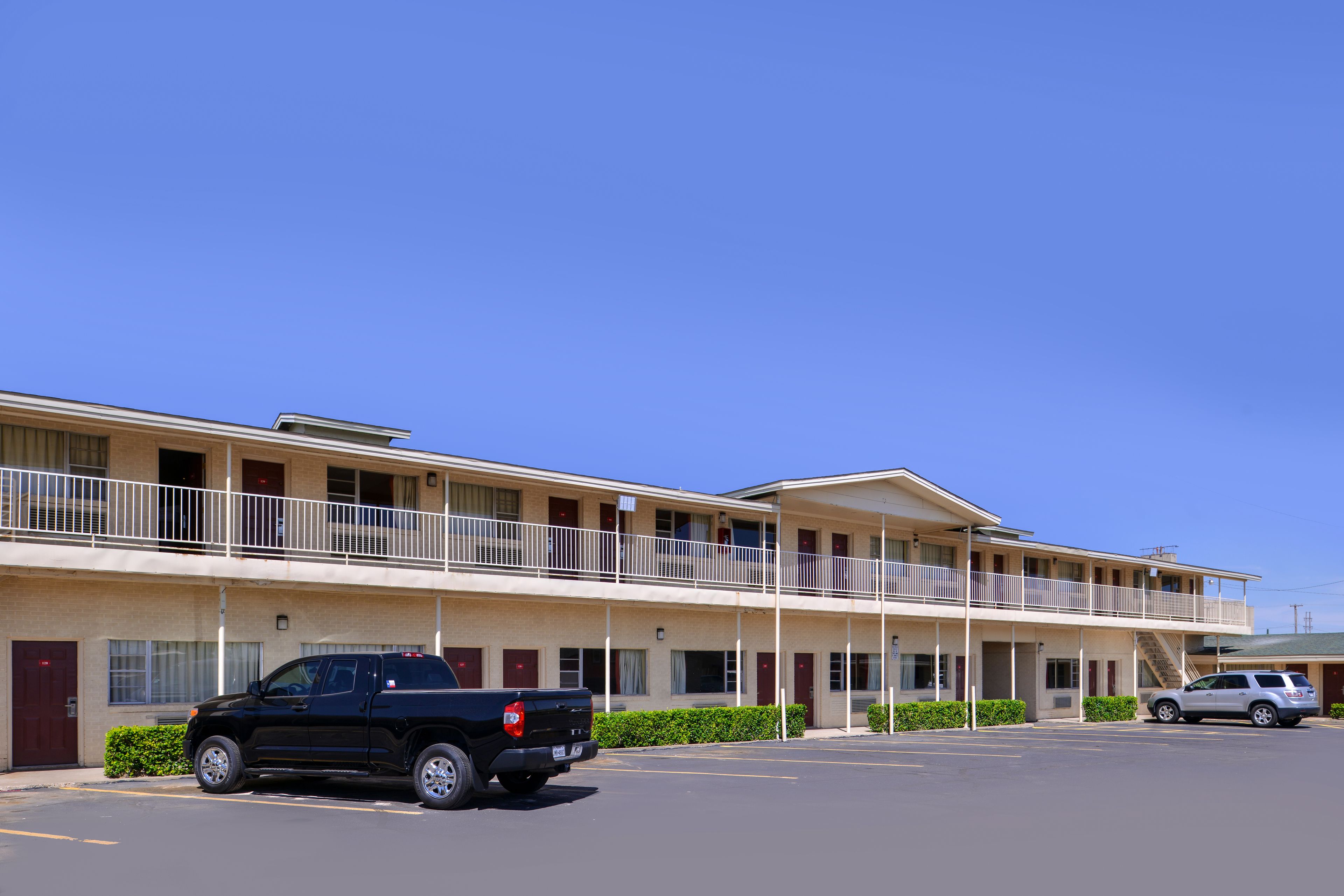 A motel with a two-story structure, a parking lot, and a black pickup truck parked in front.