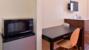 A compact kitchenette with a microwave, a small refrigerator, a telephone, and a wooden desk with a chair. - Scottish Inns & Suites (Lubbock)