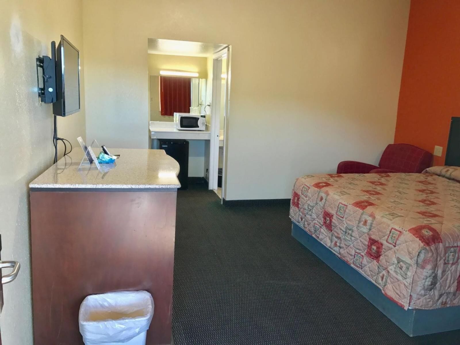 A hotel room with a bed, a desk with a chair, a microwave, and a trash bin.