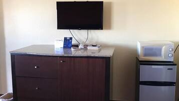 Una habitación de hotel con una cama, un escritorio con televisor, un microondas y un refrigerador pequeño.