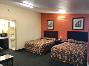 A hotel room with two beds, a desk, and a chair. There are two framed pictures on the wall.