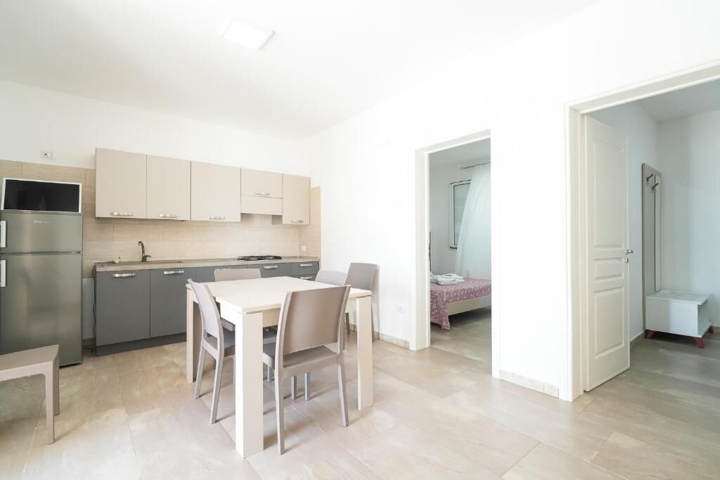 A modern kitchen with a dining table and chairs, a refrigerator, and cabinets.