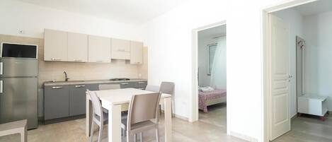 A modern kitchen with a dining table and chairs, a refrigerator, and cabinets.