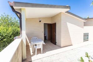 A small, single-room apartment with a tiled patio, a white table and chair, and a door leading to a bedroom. - Residence La Pineta (Otranto)