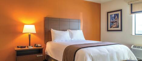 A hotel room with a bed, a nightstand with a lamp, a phone, and a picture on the wall.