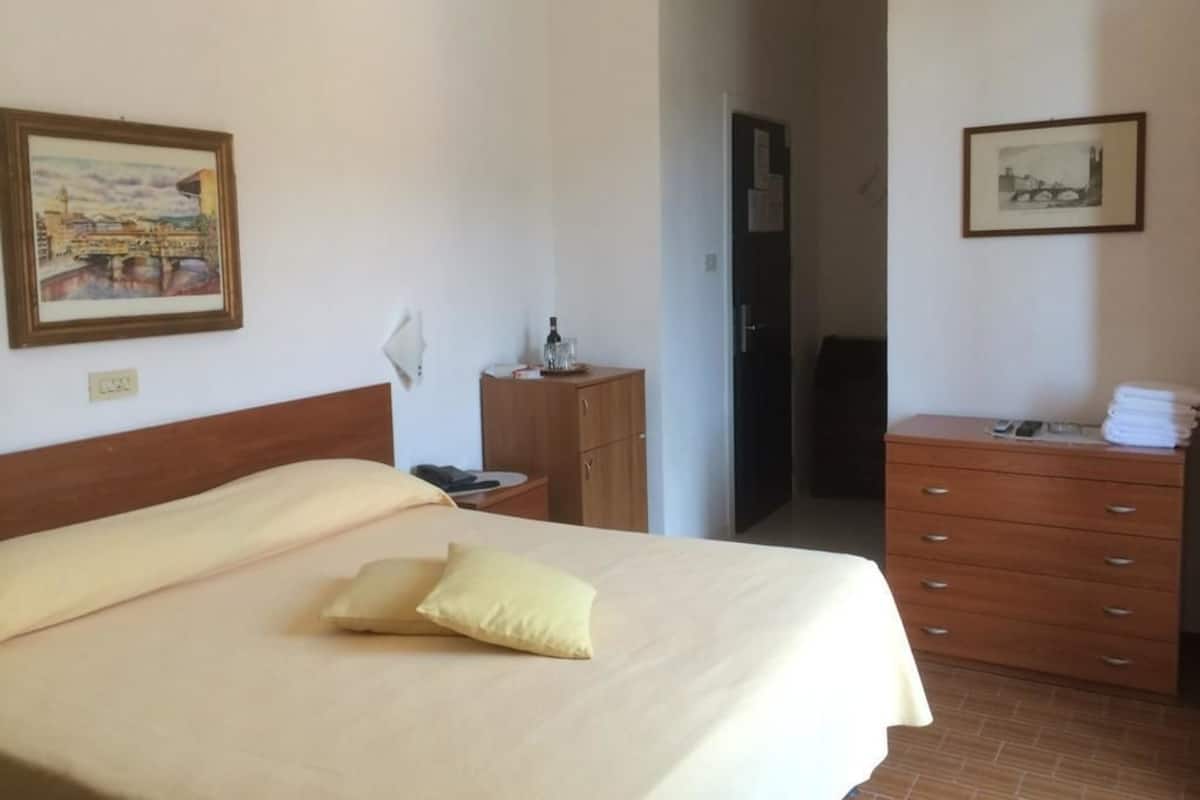 A hotel room with a bed, a wooden dresser, a nightstand, and two framed pictures on the walls.