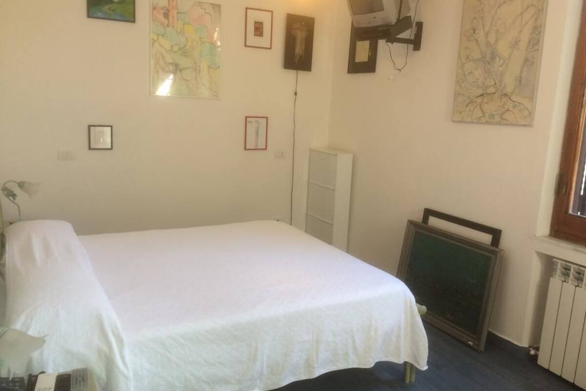 A room with a bed, a desk, a chair, a radiator, and a television mounted on the wall.