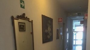 A hallway with a checkered floor, a mirror, and framed pictures on the wall. - Albergo San Carlo (Massa)
