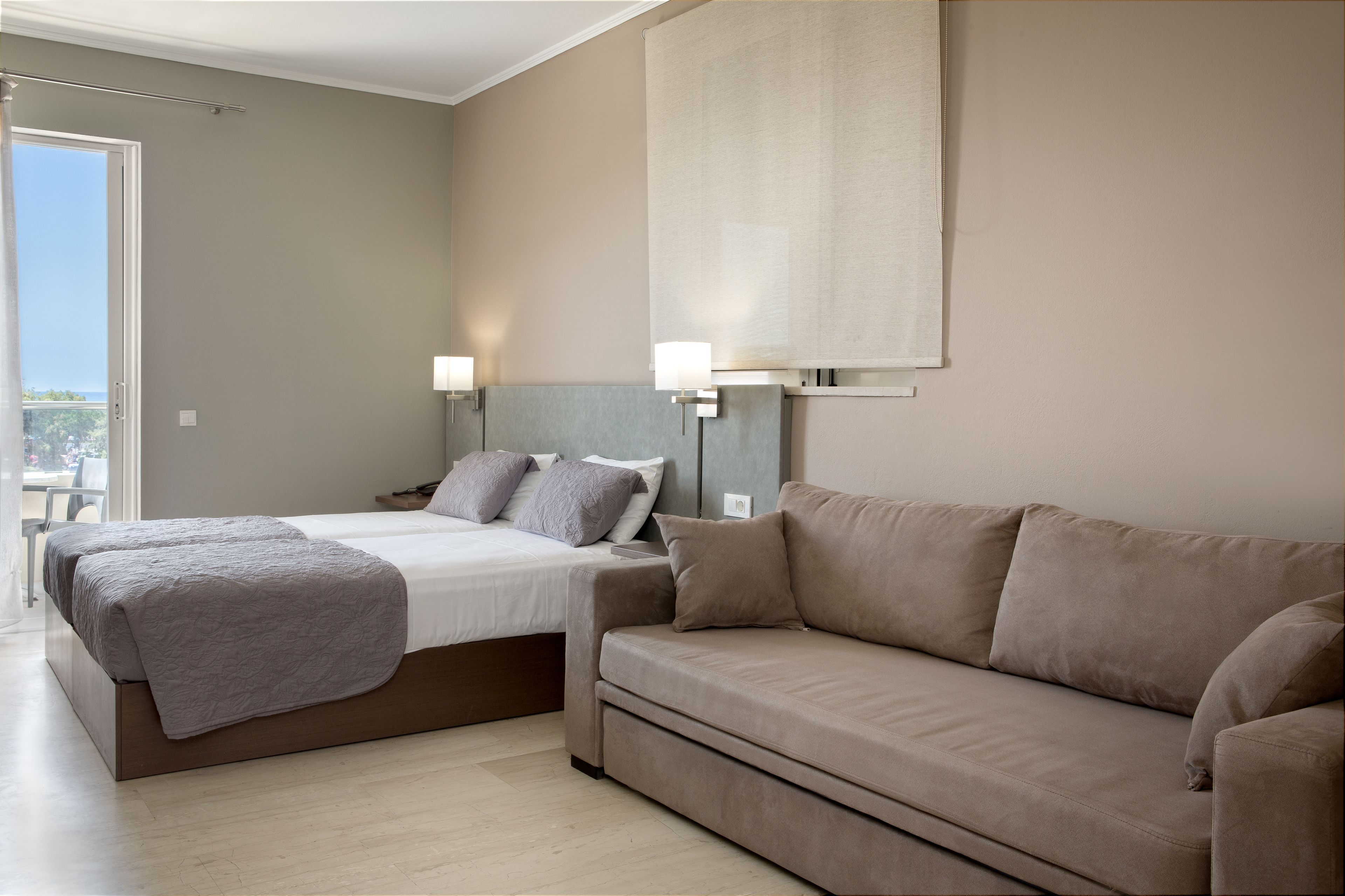 A bedroom with a bed, a sofa, and a large window.