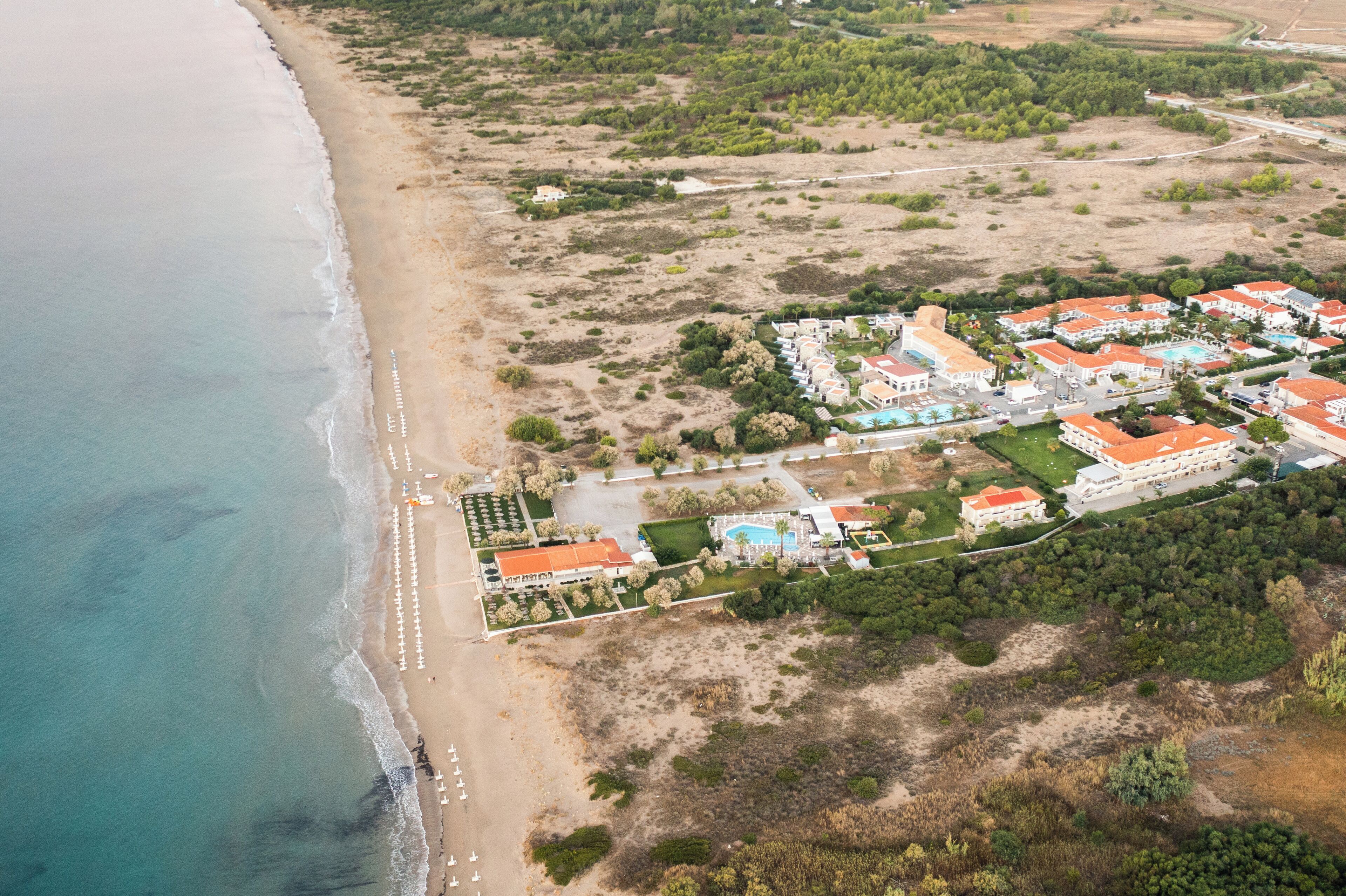 An aerial view of a coastal resort with beachfront villas, a swimming pool, and landscaped gardens.