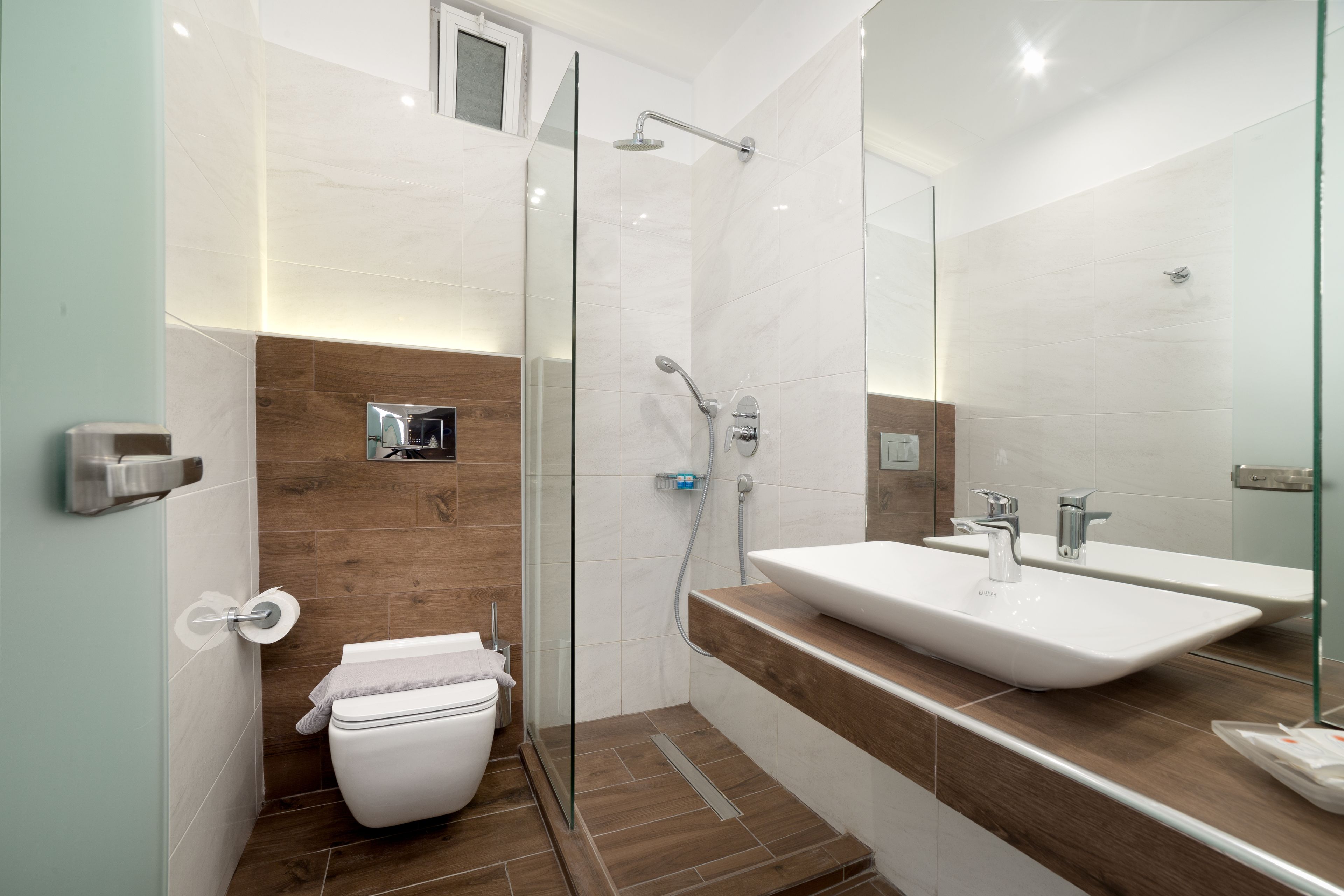 A modern bathroom with a glass shower enclosure, a white toilet, and a large sink with a mirror above it.