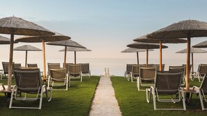 Een strandlounge met rijen ligbedden en rieten parasols, een duidelijke doorgang naar de zee en uitzicht op de oceaan.