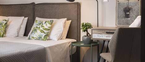 Un dormitorio ordenado con una cama, almohadas, una mesita de noche con una planta y una silla.