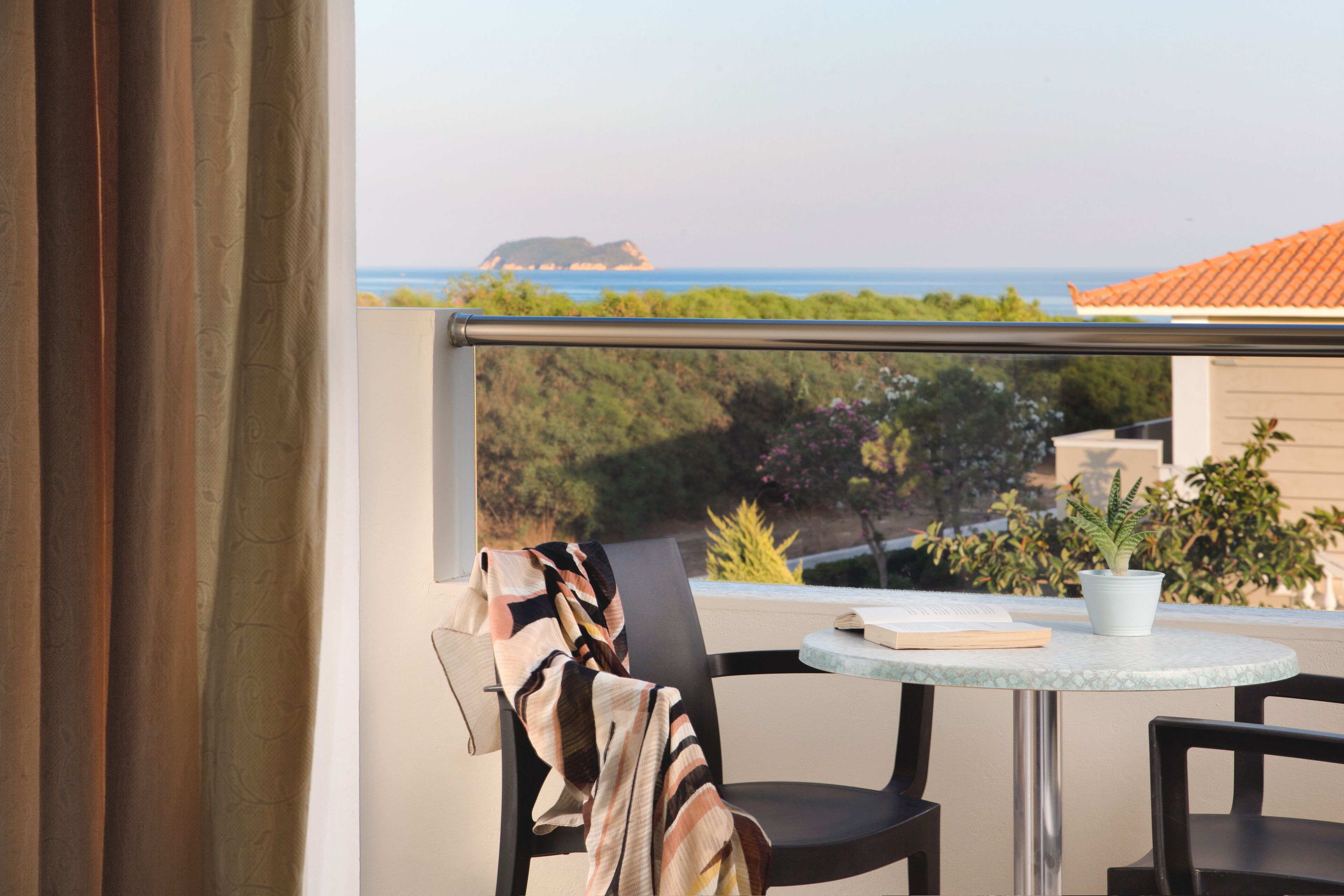 Uma varanda com vista para o mar, uma mesa com um livro e um vaso de planta.
