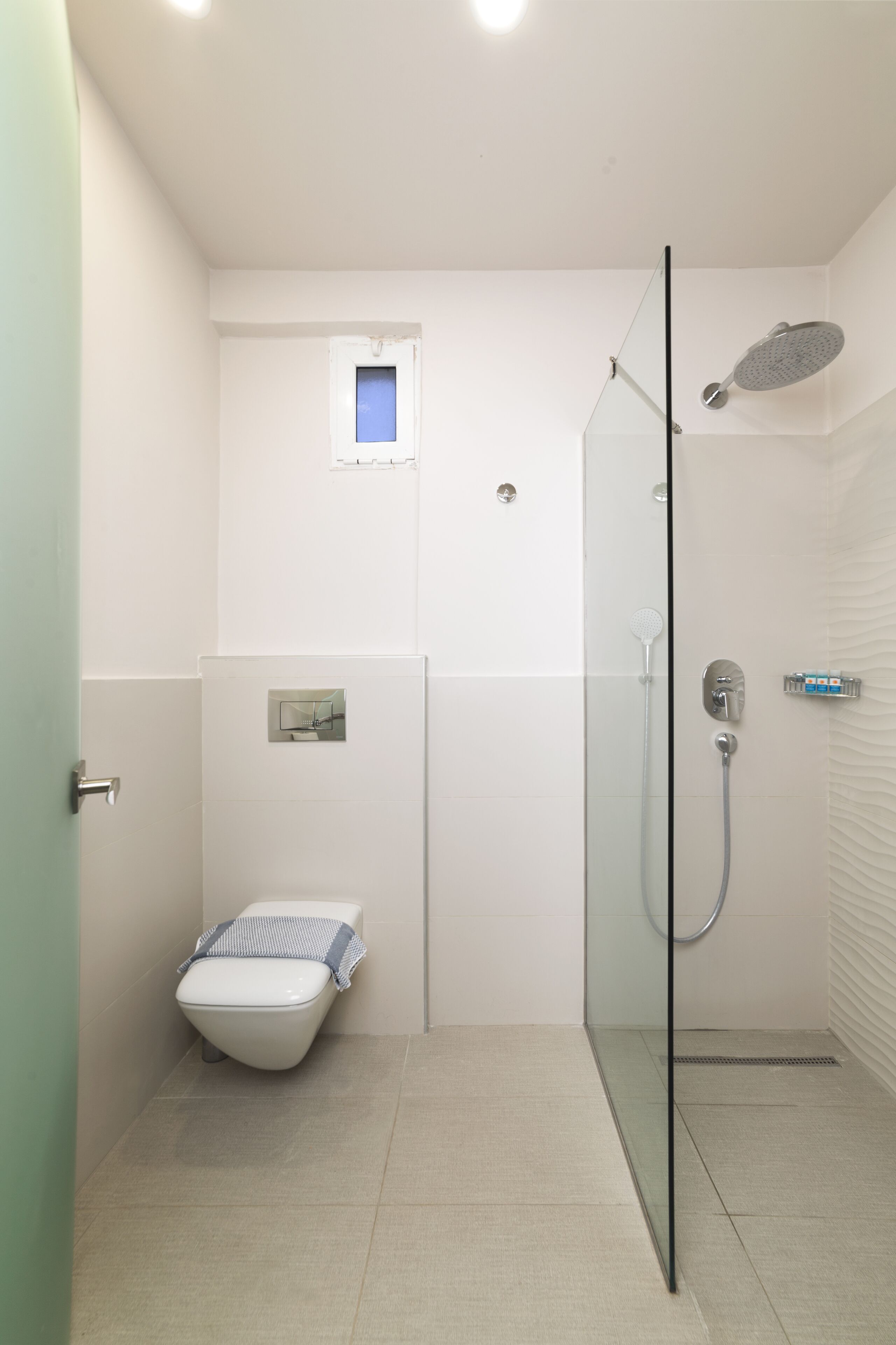 Une salle de bain moderne avec une douche à parois de verre, des toilettes et une petite fenêtre.